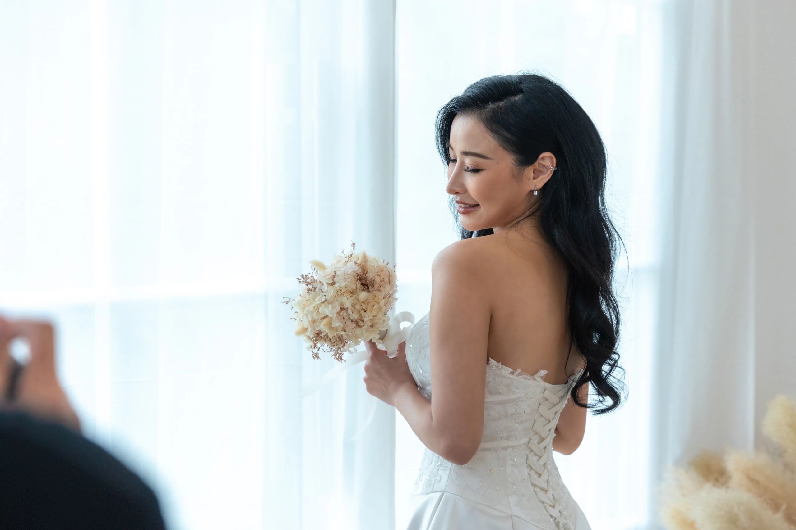 Bride in white dress holding bouquet, smiling softly.