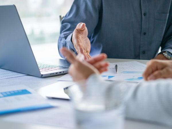 Two professionals discussing documents and working on a laptop in a business meeting.