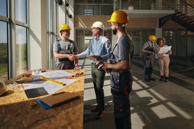 Construction workers and a manager shaking hands indoors.
