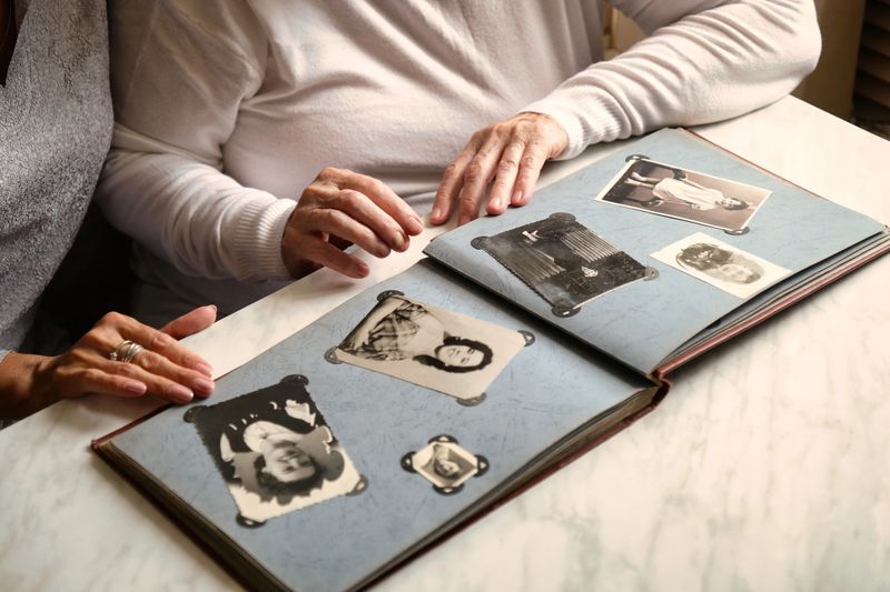 Couple looking through an old photo album filled with vintage black and white photographs, sitting at a marble table. Hands touching and pointing at the pictures. Nostalgic, family, and memory-themed image.