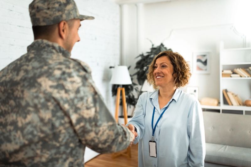 A military personnel in uniform is shaking hands with a therapist during a session, both smiling, highlighting the importance of support and connection in rehabilitation.