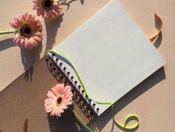 Open spiral notebook with blank pages surrounded by pink flowers and a green ribbon.