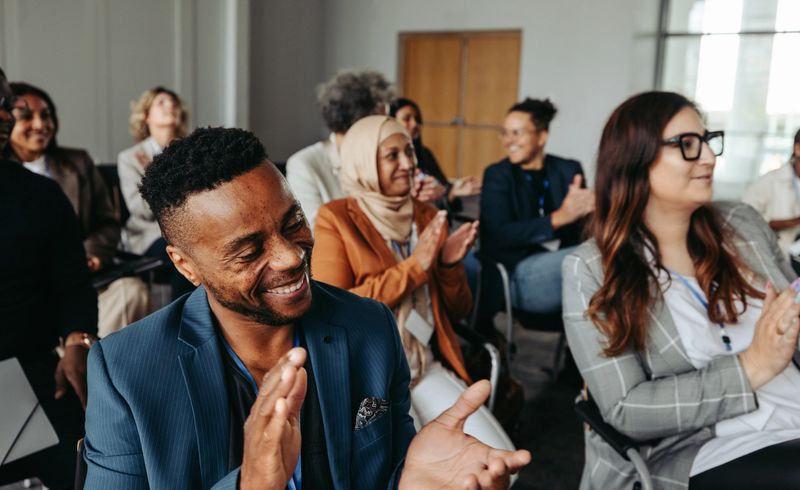 Group of smiling, multiethnic coworkers applauding during a workshop, showcasing positive engagement and teamwork.