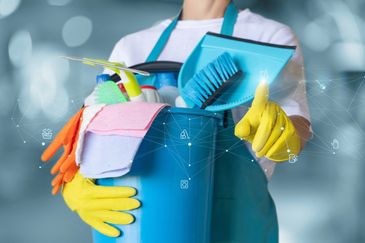 Person holding a bucket of cleaning supplies wearing yellow gloves.