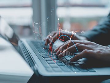 Person typing on laptop with digital warning icons and data graphs overlay.