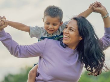 A joyful woman giving a piggyback ride to a smiling young boy outdoors.
