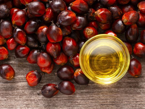 Palm oil fruit and a bowl of palm oil on a wooden surface.