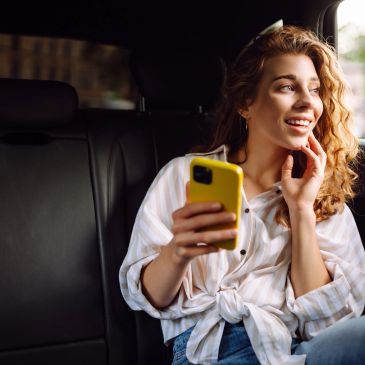 Young woman smiling while holding a yellow phone in a car.