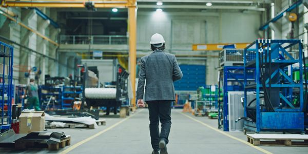 Man in a hard hat walking through a large industrial warehouse.