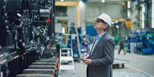 Engineer inspecting machinery in a factory while holding a tablet.