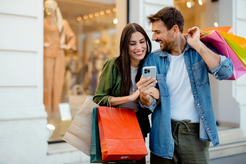 Young Happy Couple With Smart Phone and Shopping Bags in the City