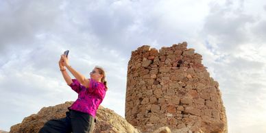 Woman taking a selfie near ancient stone ruins under a cloudy sky.