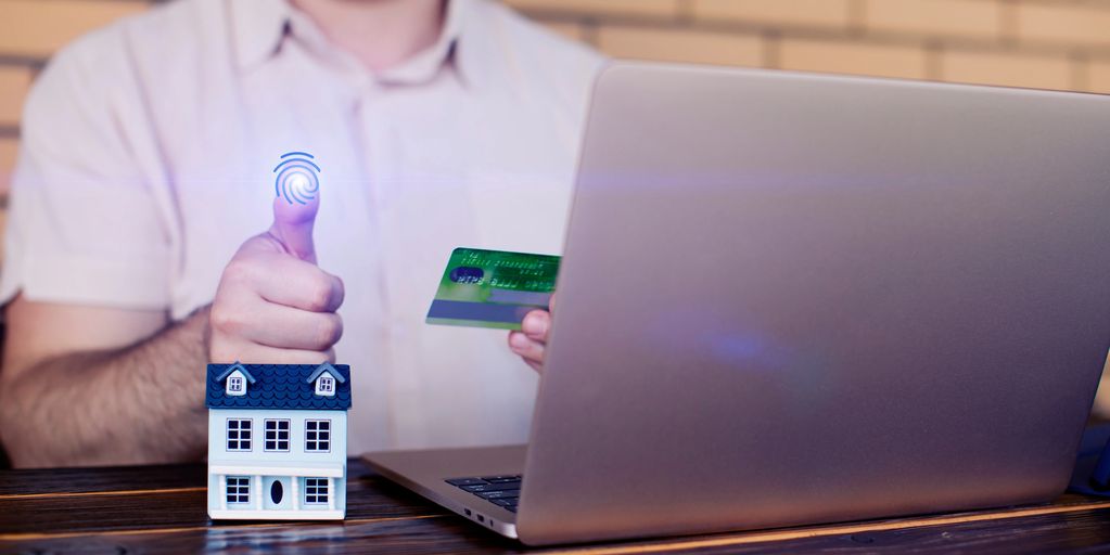 Person using fingerprint authentication for online house purchase with credit card.