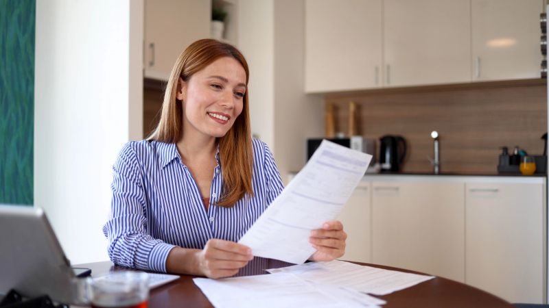 Beautiful, young woman using a digital tablet and managing her finances at home