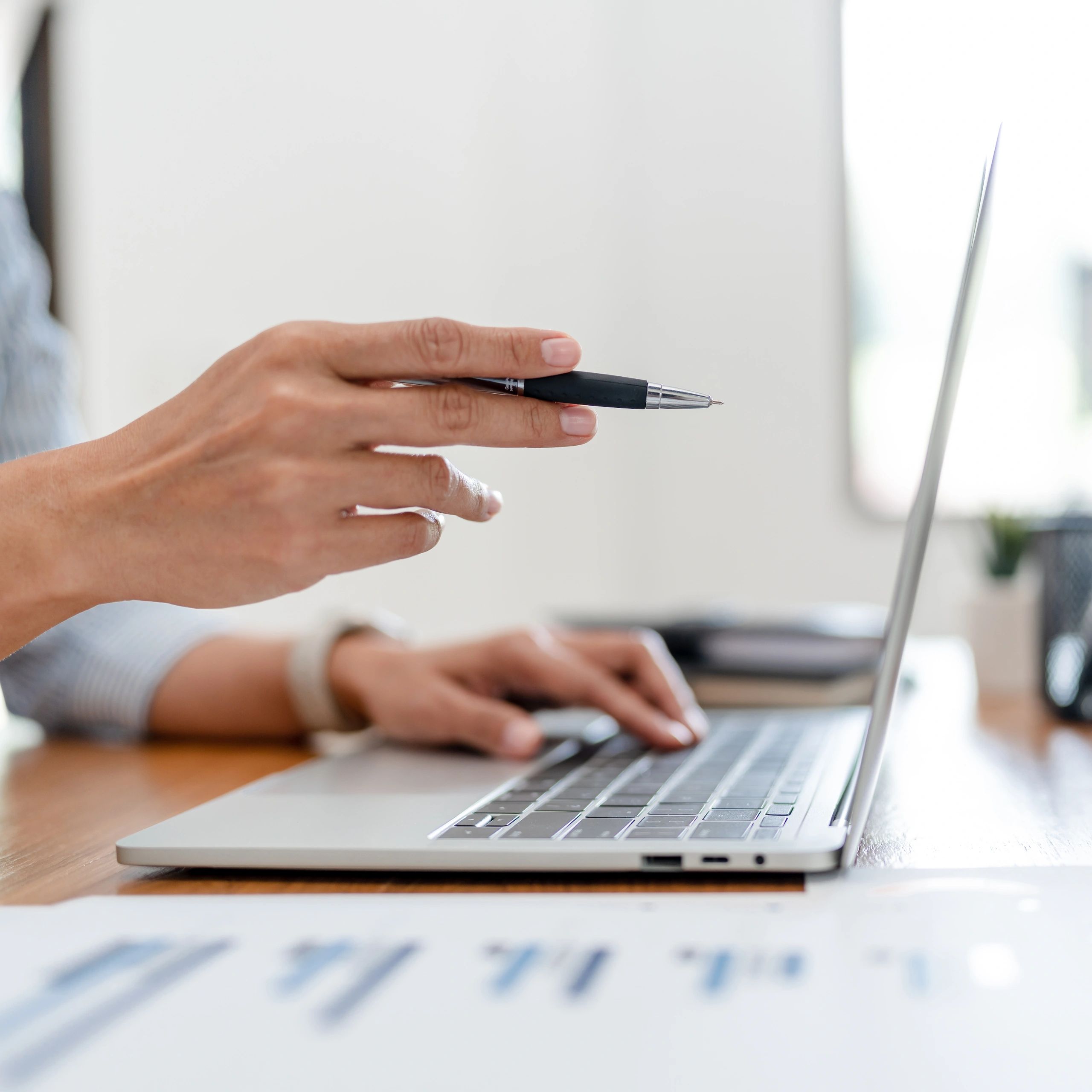 Hand holding a pen pointing at a laptop screen during a discussion.