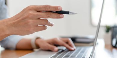 Hand holding a pen pointing at a laptop screen during a discussion.
