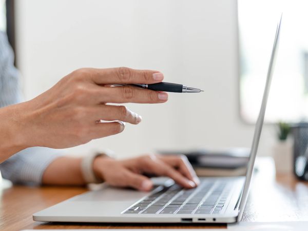 Hand holding a pen pointing at a laptop screen during a discussion.