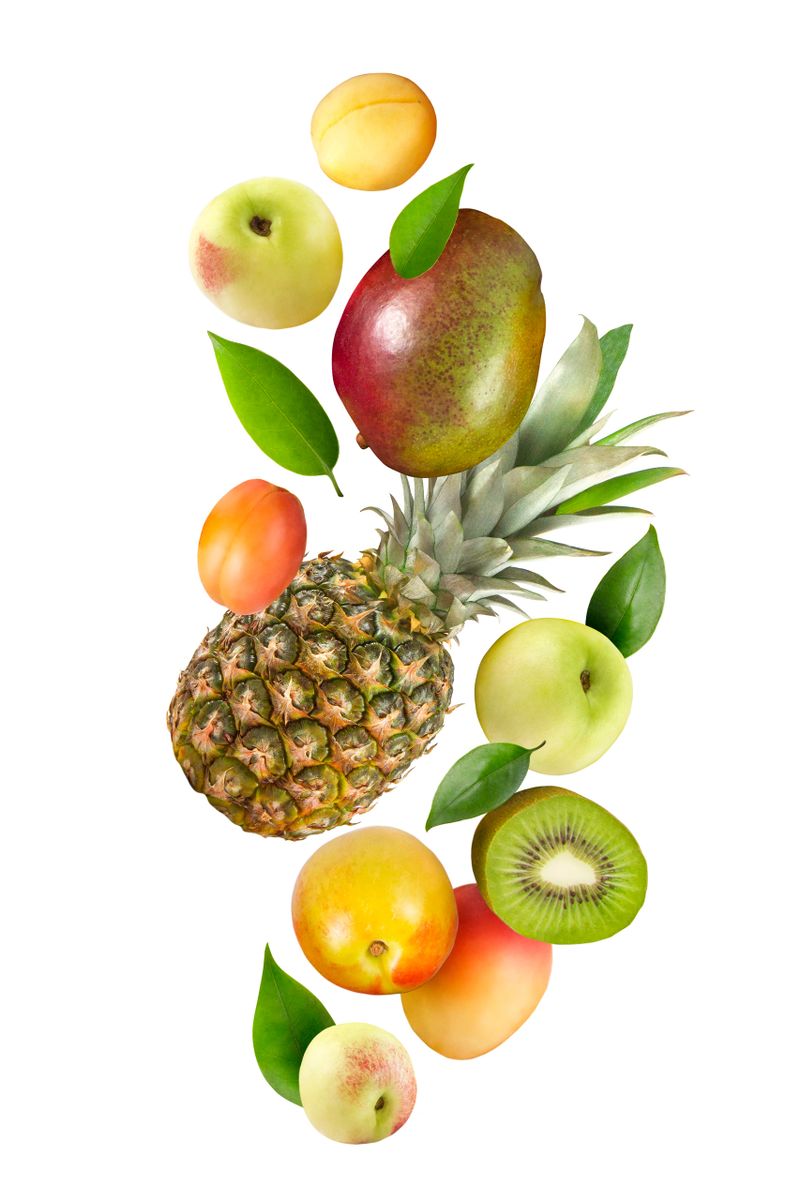 Whole and sliced tropical fruits; pineapple, mango fruit, nectarines, peaches, apricots and kiwi fruit in the air isolated on white background