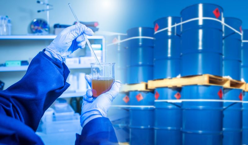 Analysis of chemical composition of oil. Laboratory assistant near barrels of fuel. Checking petroleum products for chemical composition. Lab technician holding oil sample in test tube