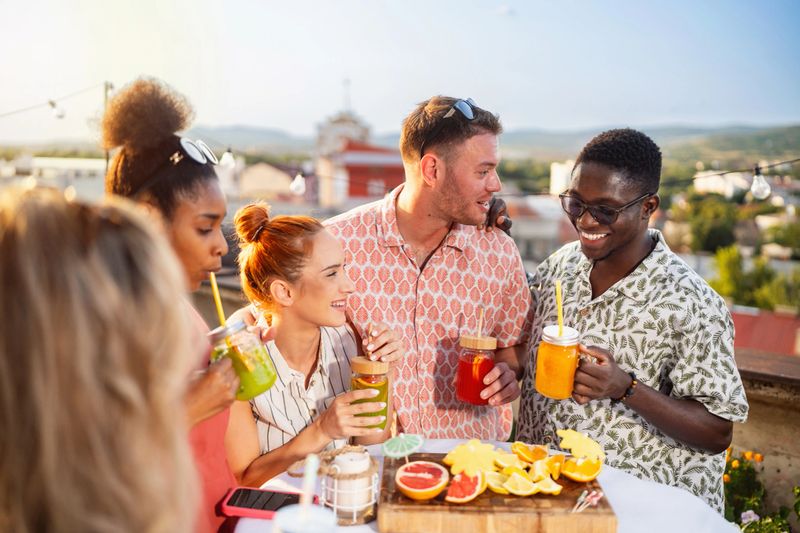 Group of modern multiracial female and male friends drinking moctkails, during a rooftop party