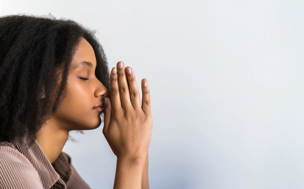 Woman with closed eyes praying with hands together.