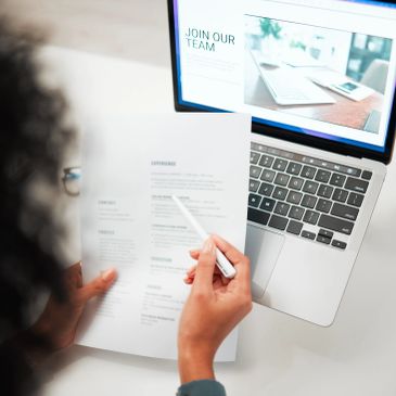 Person reviewing a document while using a laptop at a desk.
