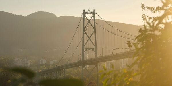 Sunlit suspension bridge with mountains in the background.