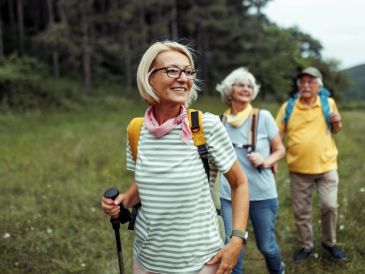 Seniors hiking outdoors with backpacks and walking sticks.