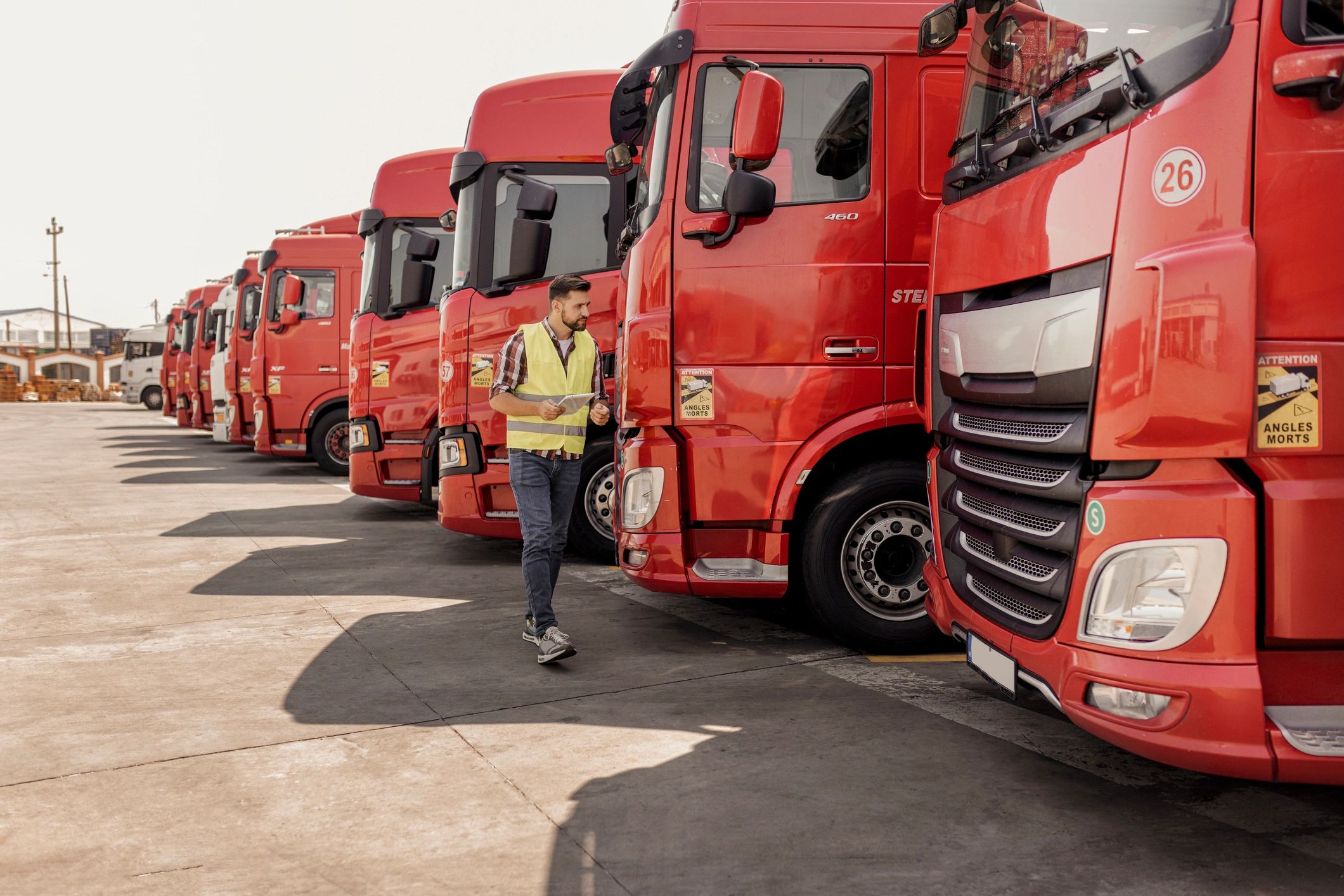 A guy in a high viz vest walking past a fleet of red trucks
