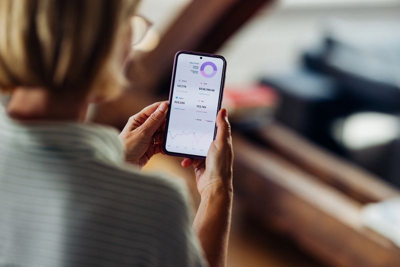 Close-up of a woman using a smartphone to review financial data and analytics at home, focusing on a detailed chart.