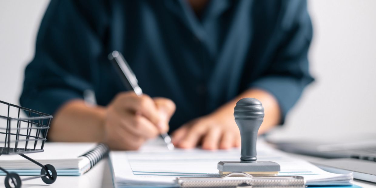 Person signing documents at a desk with a stamp in focus.