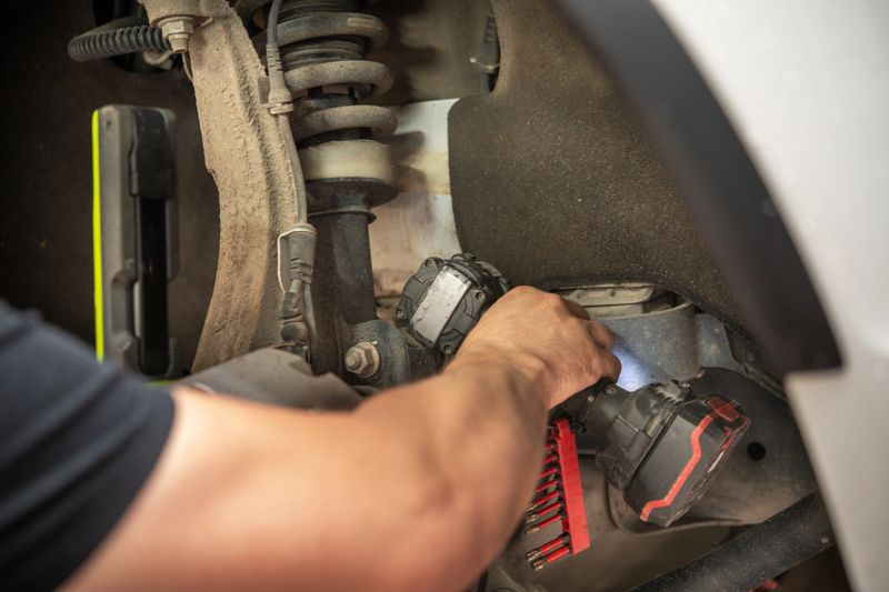 A mechanic is focused on repairing the suspension system of a car, using a power tool to ensure precision in the garage environment. The mechanic's expertise is evident in the careful adjustments made.