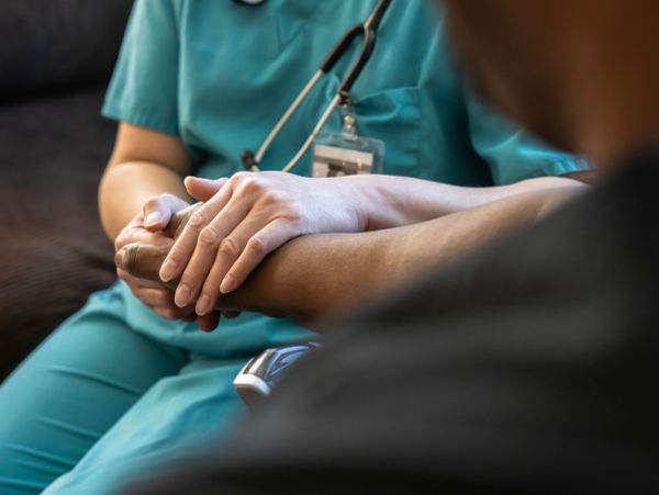Healthcare worker comforting a patient by holding hands.