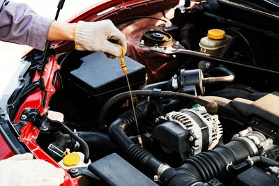 Mechanic checking engine oil level, coolant, air filter, belt, brake fluid, power steering fluid.