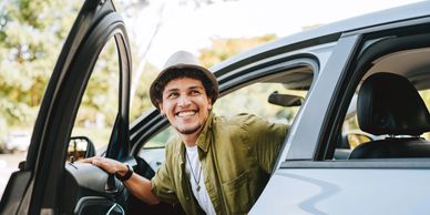 Smiling young man wearing a hat getting out of a car on a sunny day.