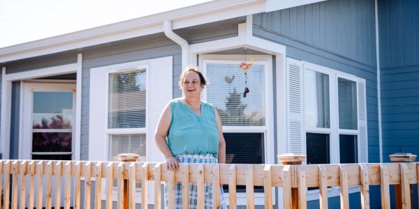 A woman standing on a wooden deck outside a blue and white house.