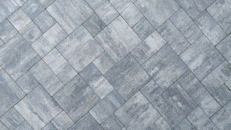 A close-up view of a gray paved surface arranged in a herringbone pattern, showcasing its textured design and color variations.