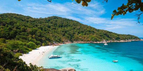 A tropical beach with clear blue water and boats.
