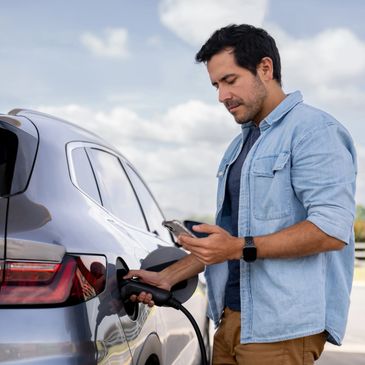 Man charging an electric car using a charging station outdoors.