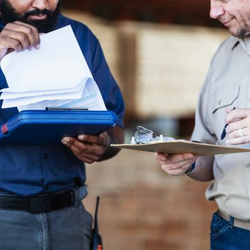 Two men reviewing documents on clipboards in a work setting.