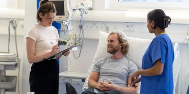 Patient in hospital bed talking with a nurse and a woman with a clipboard.