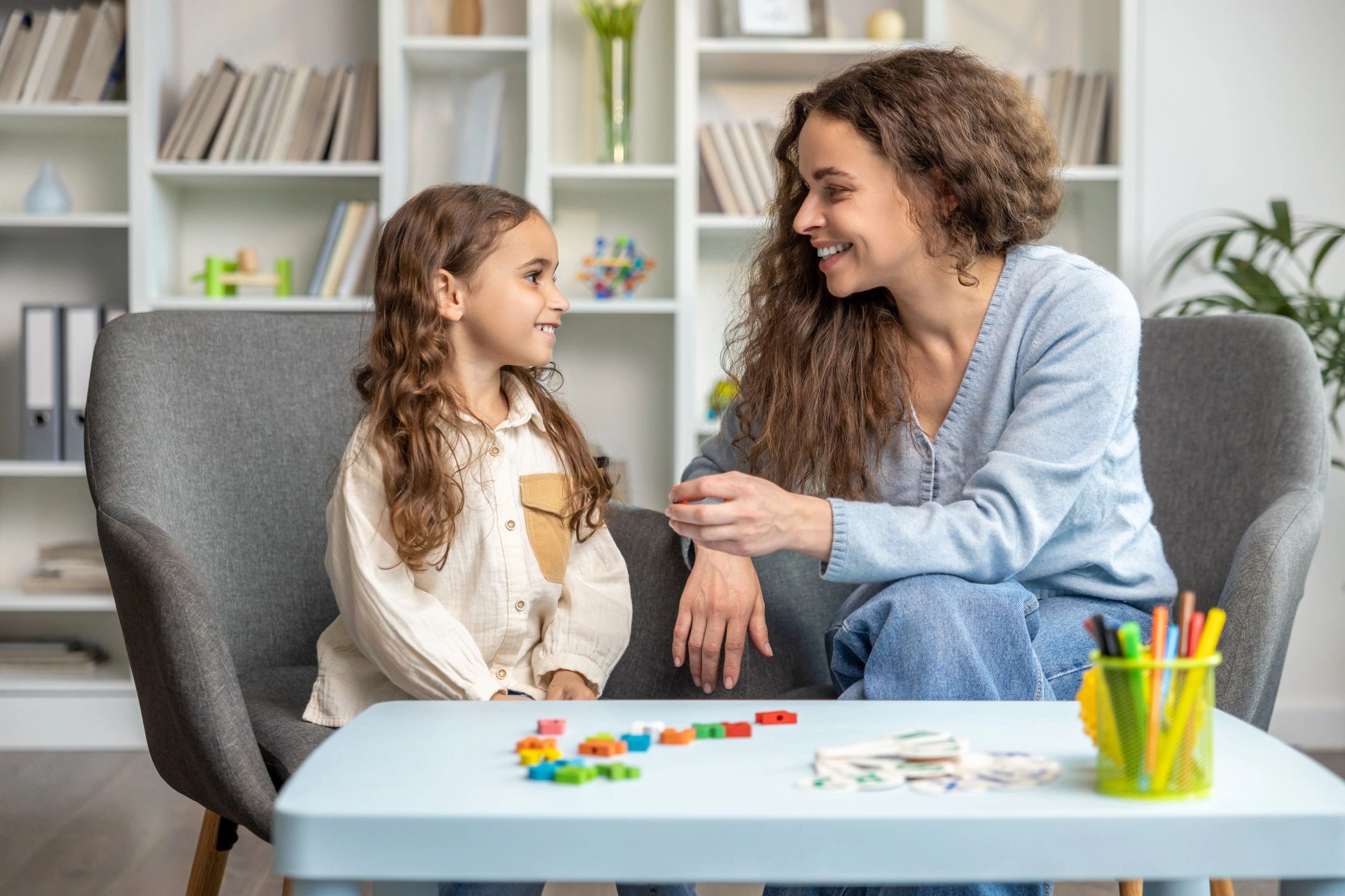A woman and a girl smiling at each other while sitting in a cozy room.