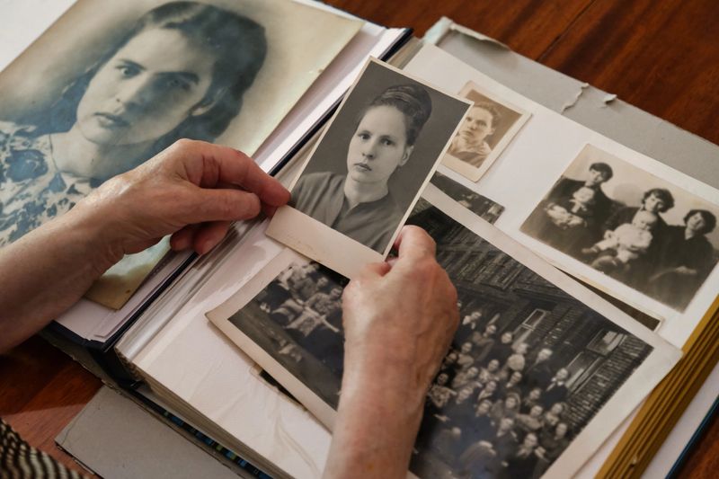 Close-up of elderly person’s hands holding black-and-white photographs from vintage photo album.
