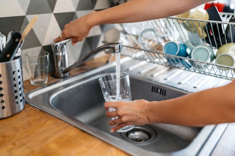 Young woman filling a glass of water in the sink. Close-up.