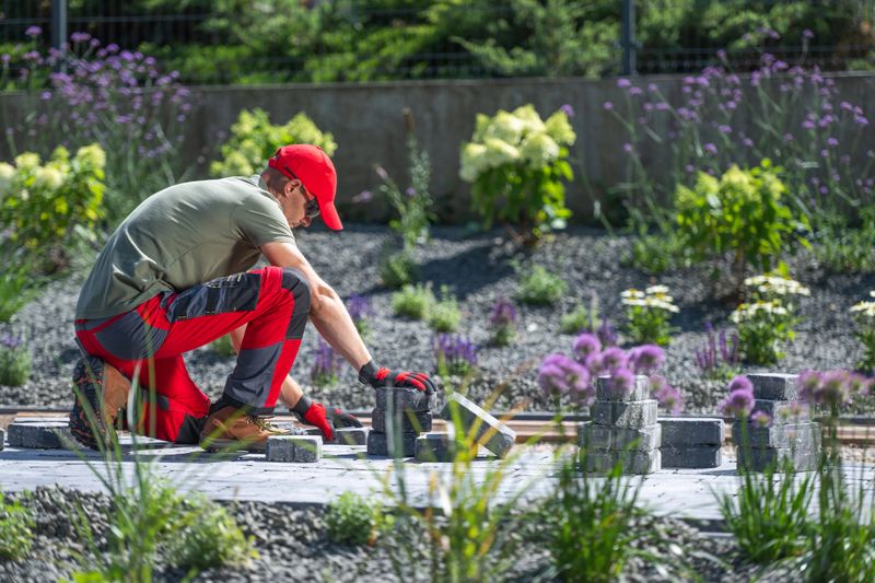 A gardener carefully arranges stones to create a pathway amidst vibrant flowers on a bright day.