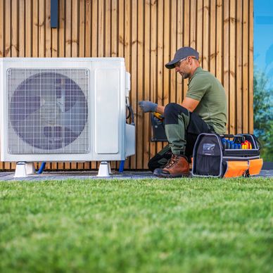 Technician repairing an outdoor HVAC unit next to a wooden wall.