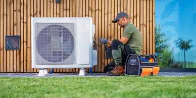Technician repairing an outdoor air conditioning unit beside a wooden wall.