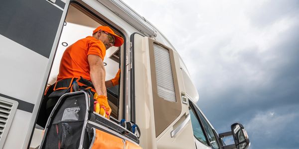 Technician entering RV with a toolbox under cloudy sky.