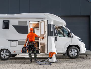 Technician entering a motorhome with tools to repair and a vacuum cleaner outside.