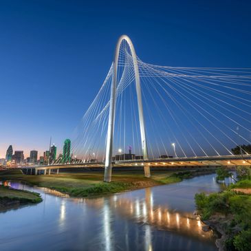 The Margaret Hunt Hill Bridge in Dallas at dusk, illuminated and reflecting on the Trinity River.